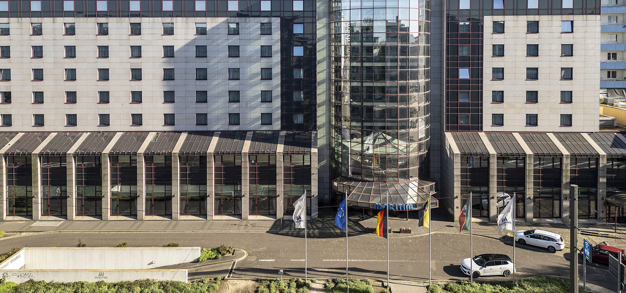 Frontansicht des Maritim Hotels mit moderner Glasfassade und Flaggen am Eingang, zeigt die zentrale und repräsentative Architektur.