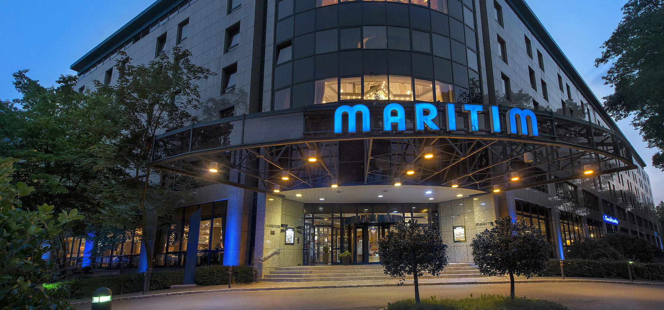Außenansicht des Maritim Hotel Bremen bei Dämmerung, beleuchtetes Logo und moderne Architektur.