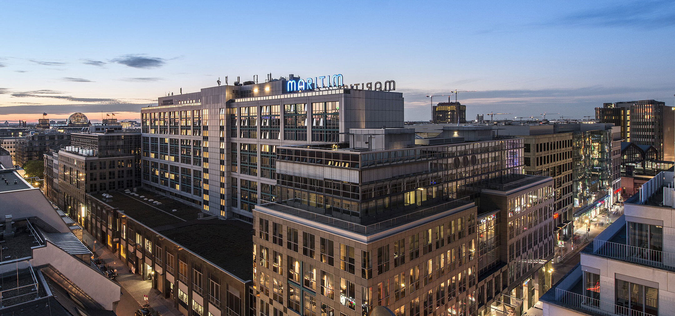 Blick auf das Maritim proArte Hotel Berlin bei Dämmerung, umgeben von modernen Gebäuden im Herzen Berlins.