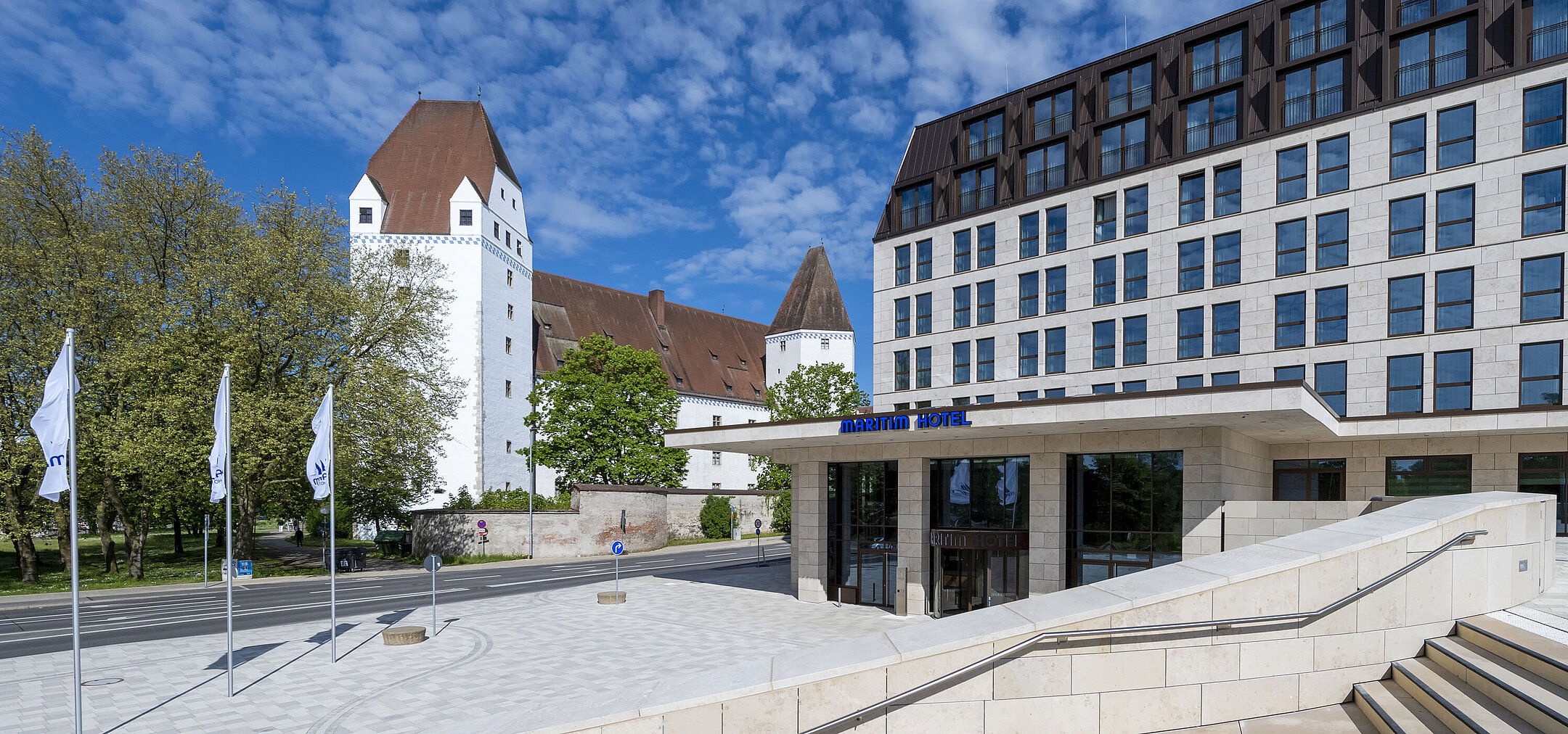 Das moderne Maritim Hotel Ingolstadt mit dem historischen Neuen Schloss im Hintergrund und einladendem Eingangsbereich.