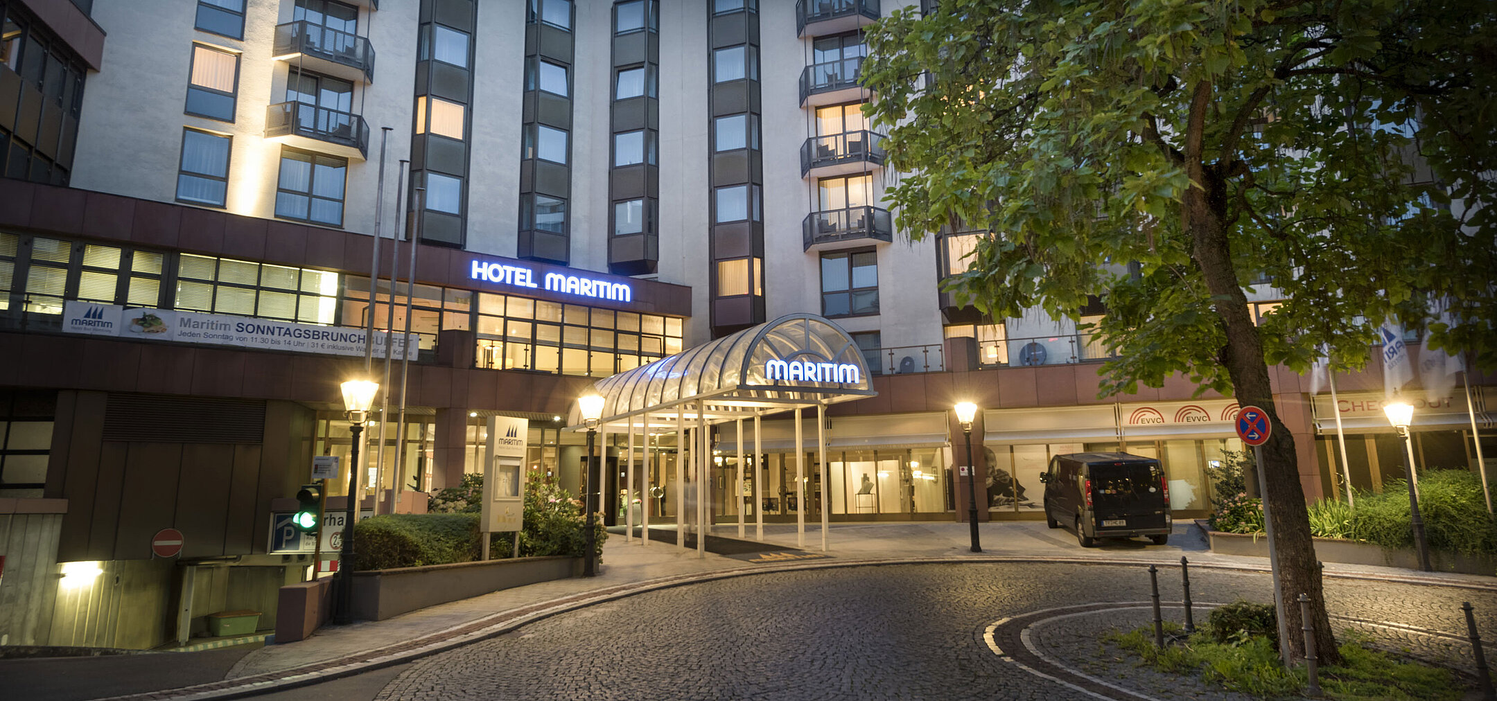 Stimmungsvoller Hoteleingang des Maritim Hotel Bad Homburg in der Abenddämmerung mit Beleuchtung.